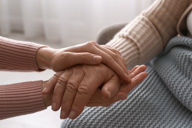 Young and elderly women holding hands together indoors, closeup