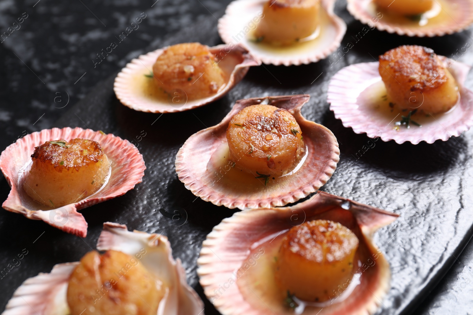 Photo of Delicious fried scallops in shells on black table, closeup