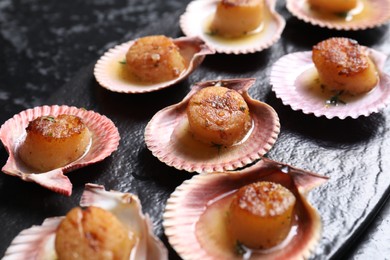 Photo of Delicious fried scallops in shells on black table, closeup