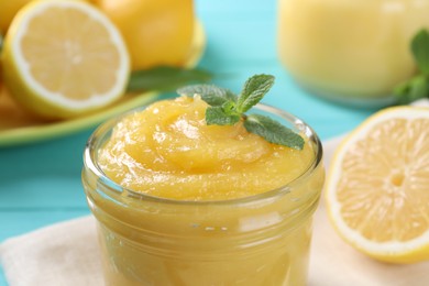 Delicious lemon curd in glass jar and mint on light blue table, closeup