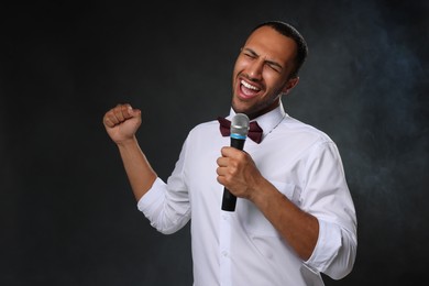 Handsome man with microphone singing on black background