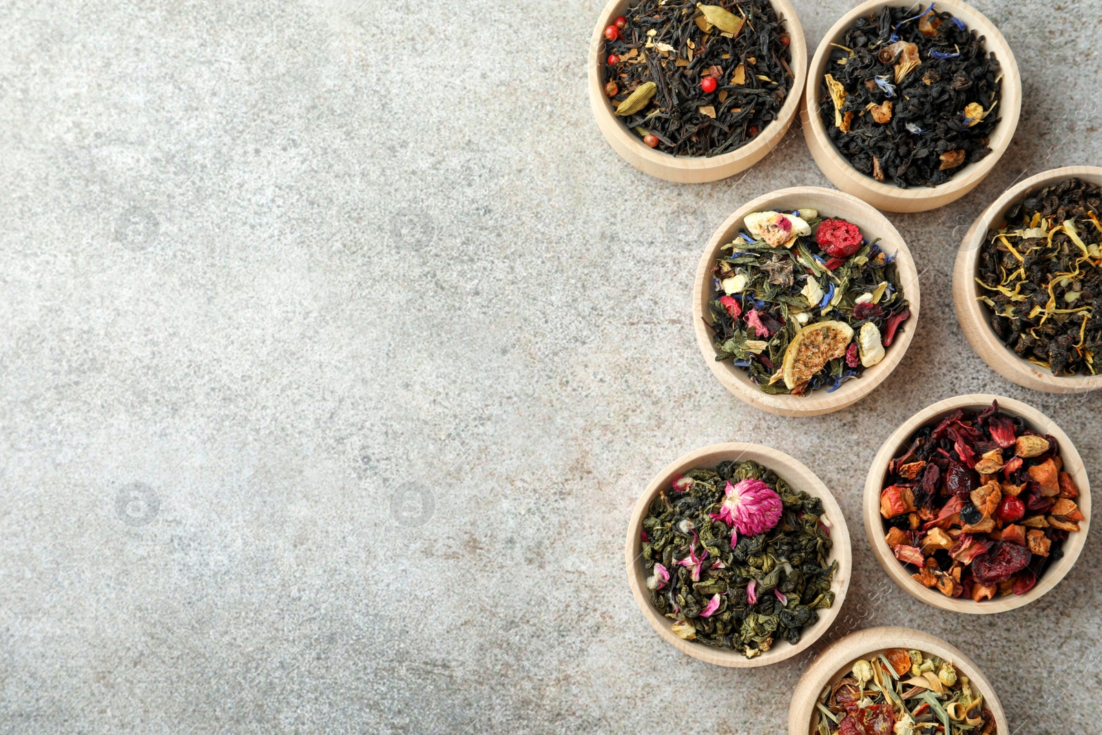 Photo of Different kinds of dry herbal tea in wooden bowls on light grey table, flat lay. Space for text