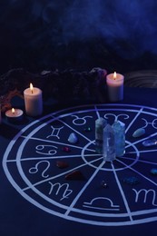 Photo of Natural stones for zodiac signs, drawn astrology chart and burning candles on black table. Color tone effect