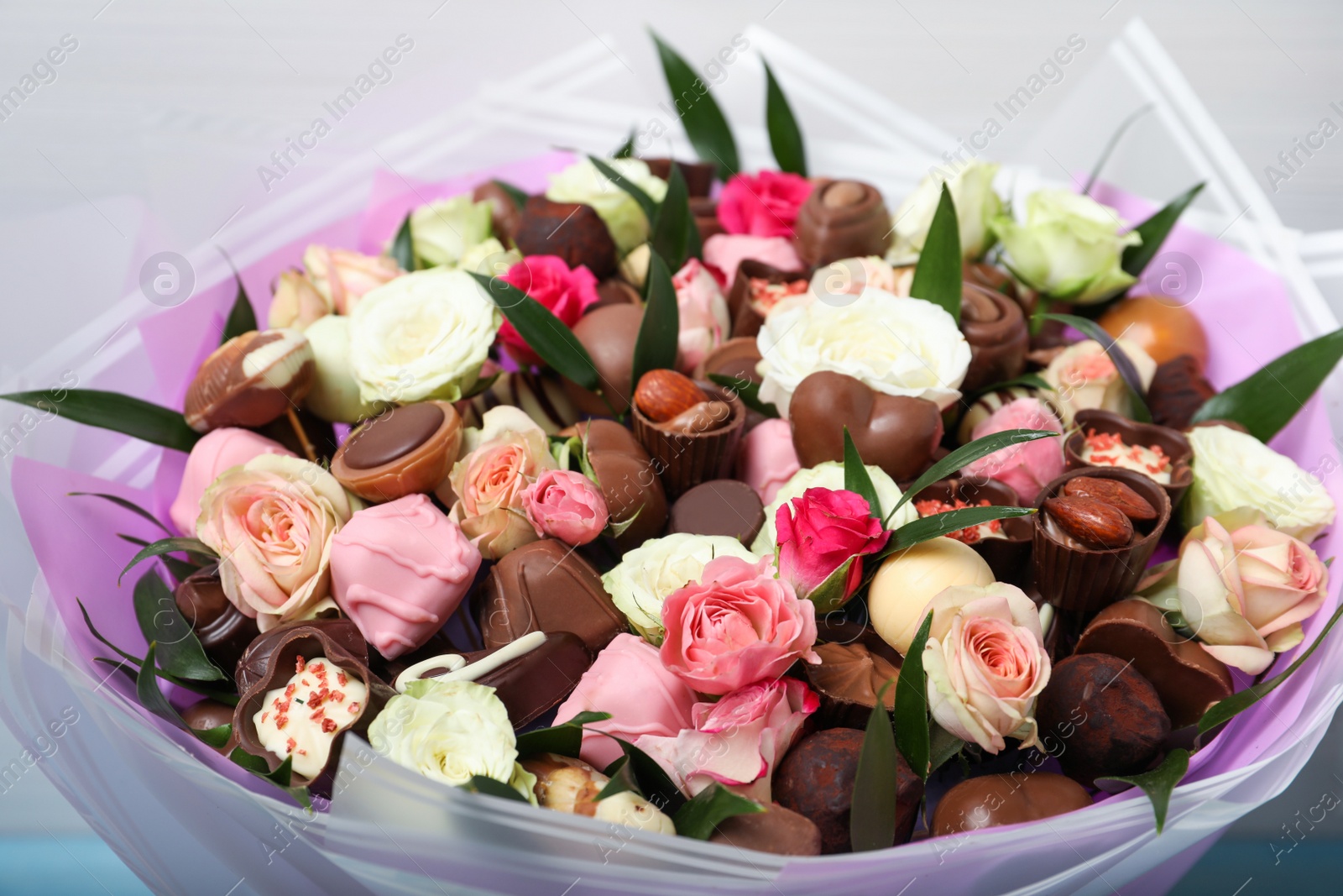 Photo of Beautiful bouquet of flowers and chocolate candies on light background, closeup