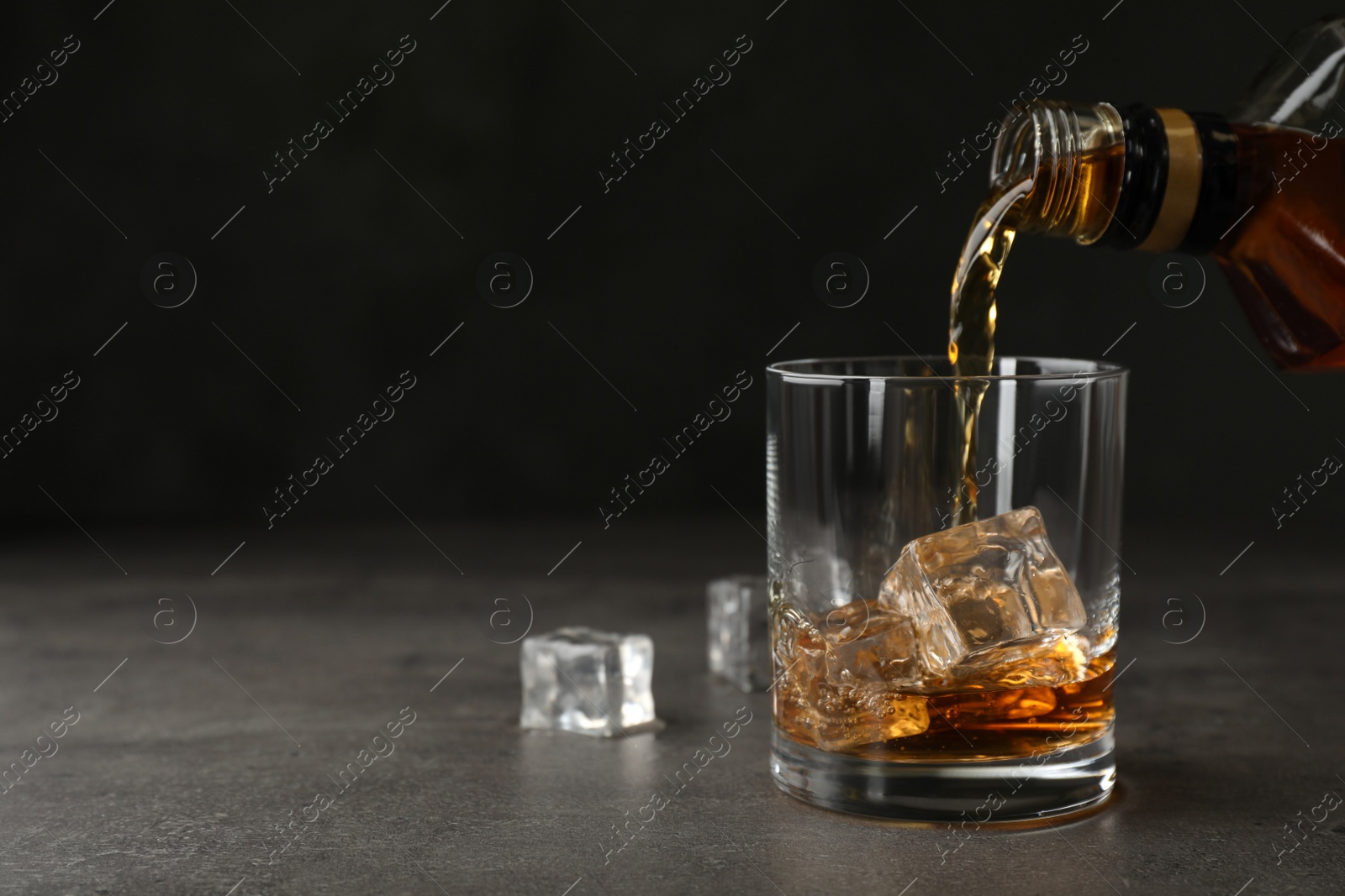 Photo of Pouring whiskey from bottle into glass with ice cubes on table. Space for text