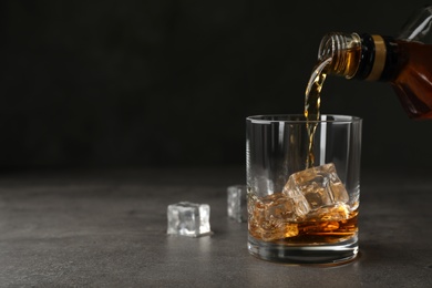 Pouring whiskey from bottle into glass with ice cubes on table. Space for text