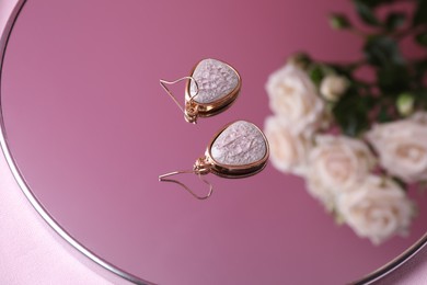 Photo of Beautiful earrings on mirror with flowers reflection
