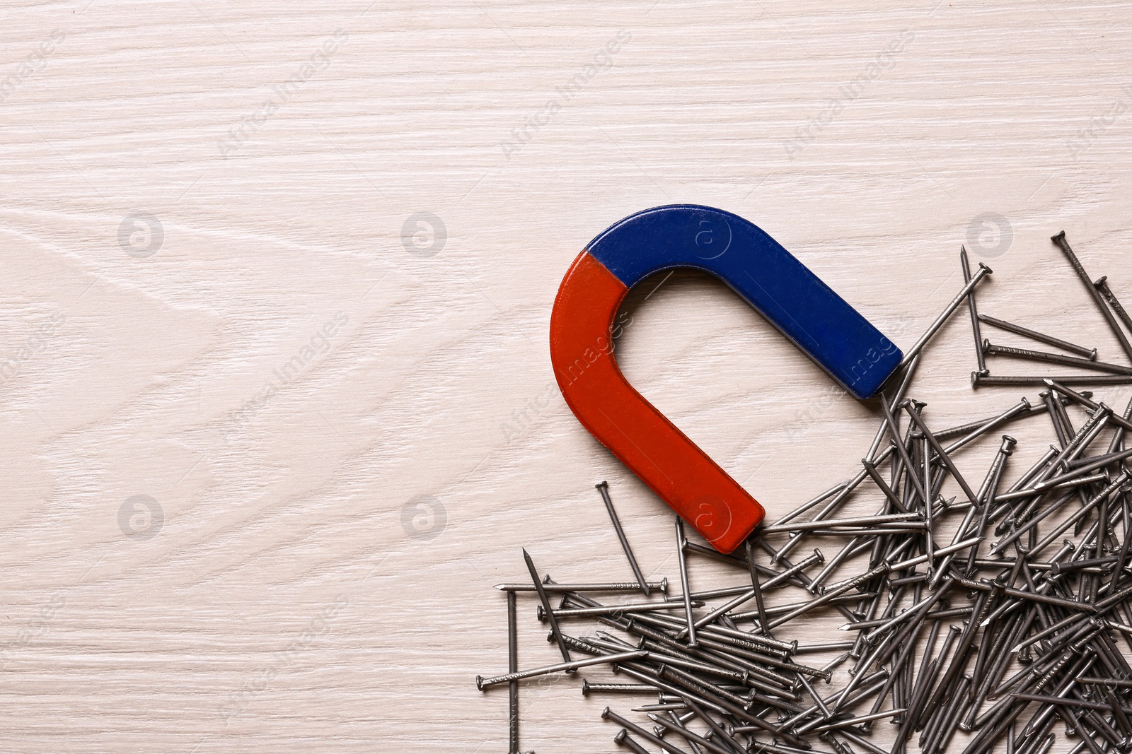 Photo of Magnet attracting nails on light wooden background, flat lay. Space for text