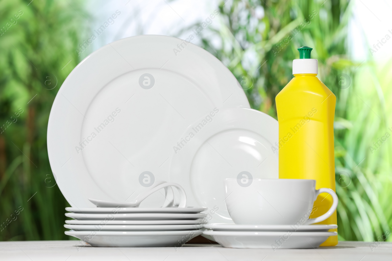 Photo of Set of clean dishware and detergent on white table against blurred background