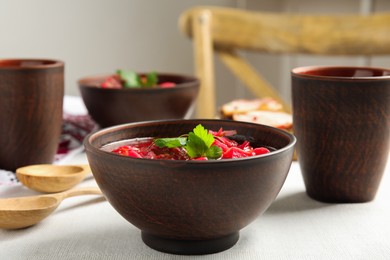 Stylish brown clay bowl with Ukrainian borsch served on white tablecloth