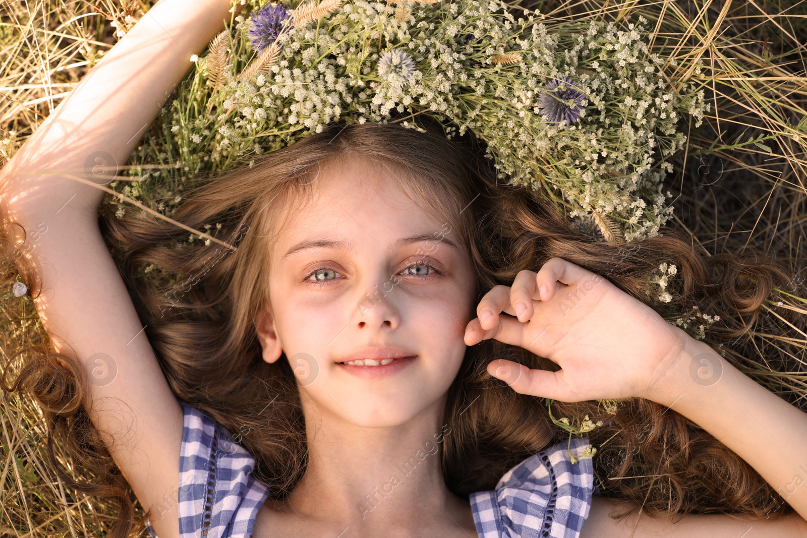 Photo of Cute little girl wearing wreath made of beautiful flowers on green grass, top view