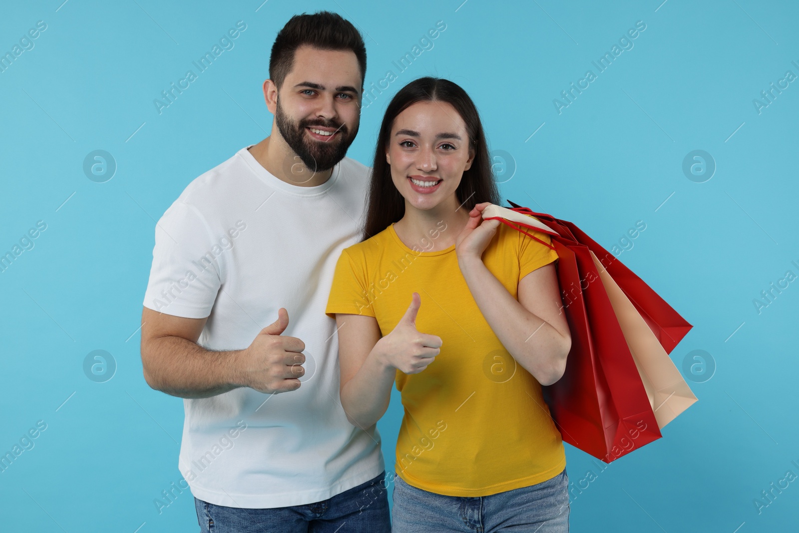 Photo of Happy couple with shopping bags showing thumbs up on light blue background