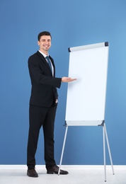 Photo of Business trainer giving presentation on flip chart board against color wall background