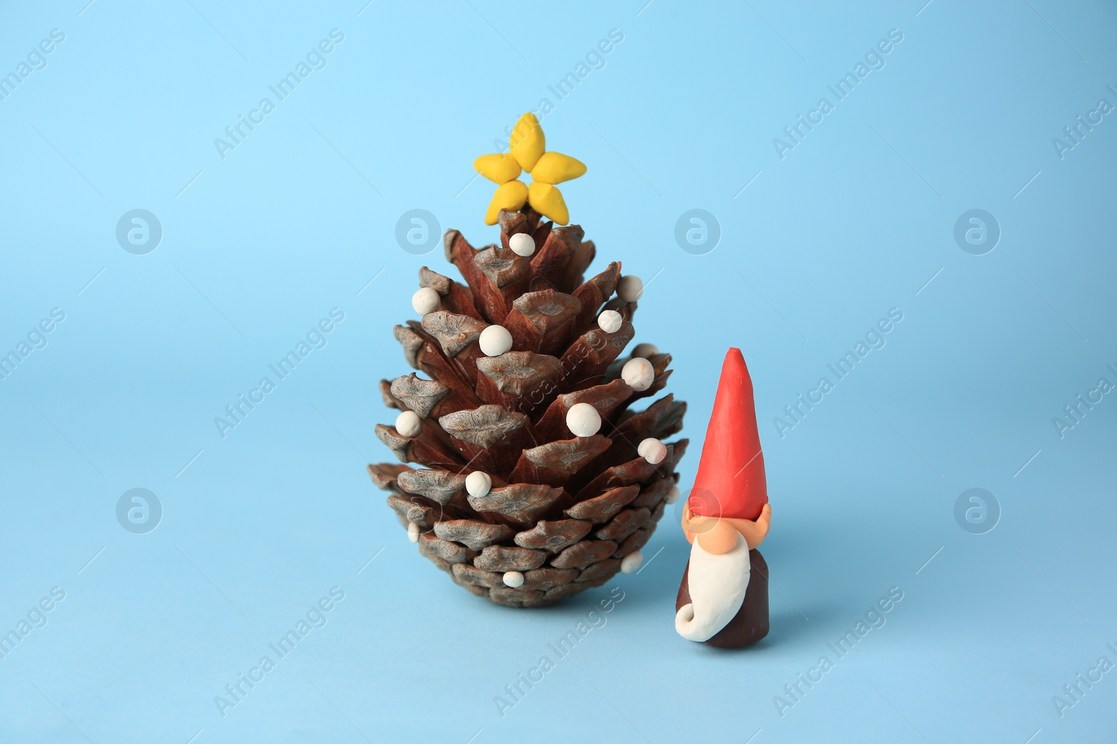 Photo of Beautiful plasticine dwarf with pinecone on light blue background. Children's handmade ideas