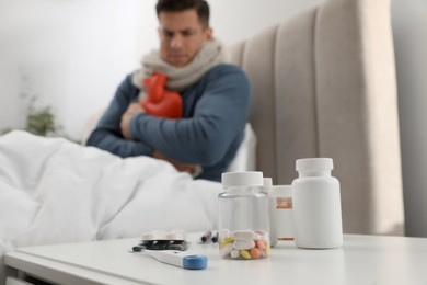 Photo of Ill man with hot water bottle at home, focus on pills