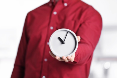 Young man holding alarm clock on blurred background. Time concept