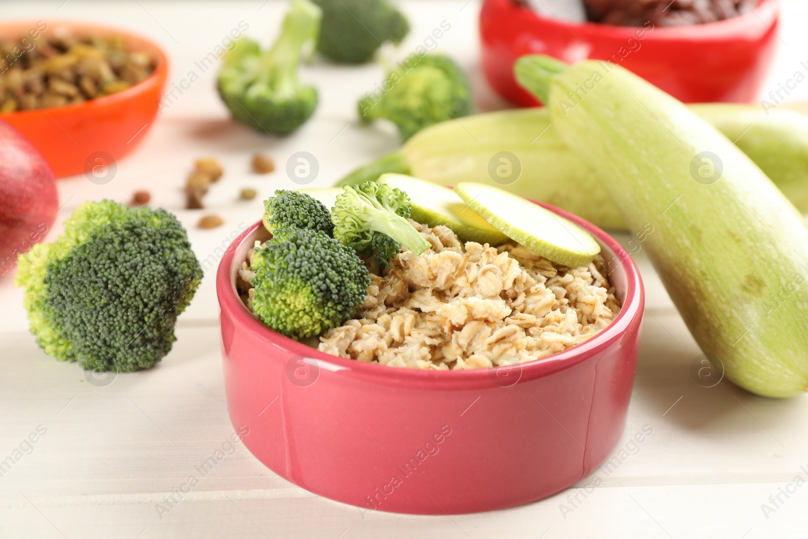 Photo of Feeding bowl with oatmeal porridge and vegetables on white wooden table, closeup. Natural pet food