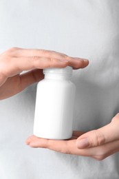 Photo of Woman holding one white pill bottle, closeup