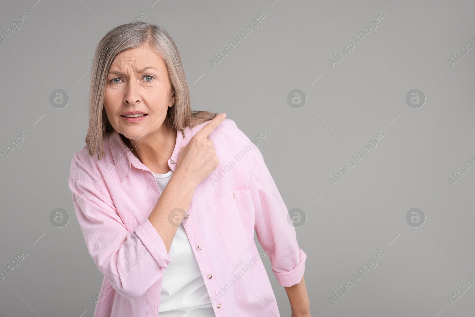 Photo of Surprised senior woman pointing at something on grey background, space for text