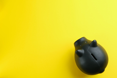 Photo of Black piggy bank on yellow background, top view. Space for text