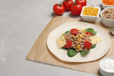 Photo of Delicious tortilla with tuna, vegetables and cheese on light table, space for text. Cooking shawarma