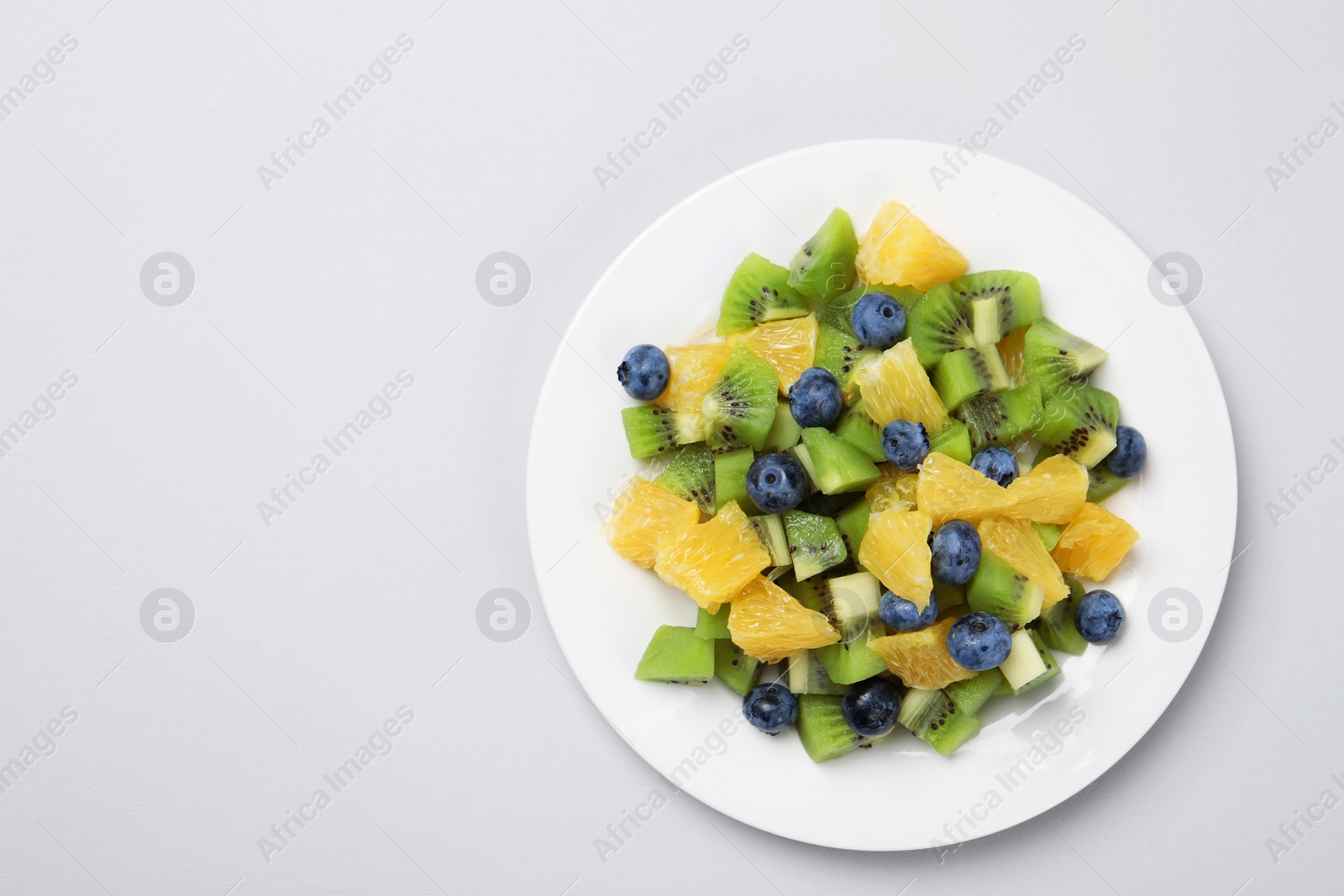 Photo of Plate of tasty fruit salad on light grey background, top view. Space for text