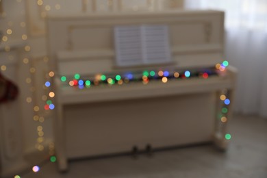 Photo of Blurred view of white piano with fairy lights indoors. Christmas music
