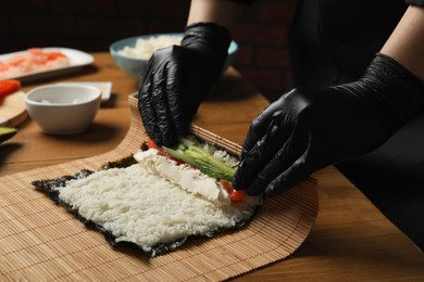 Photo of Chef in gloves making sushi roll at wooden table, closeup