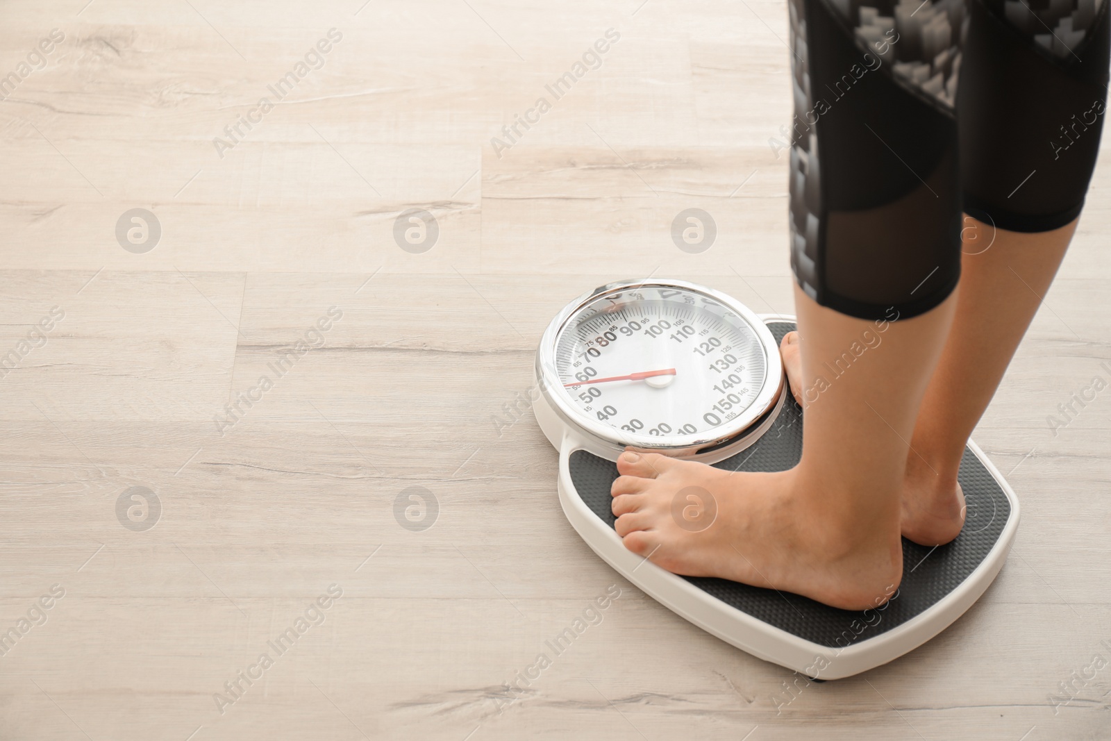 Photo of Woman measuring her weight using scales on wooden floor. Healthy diet