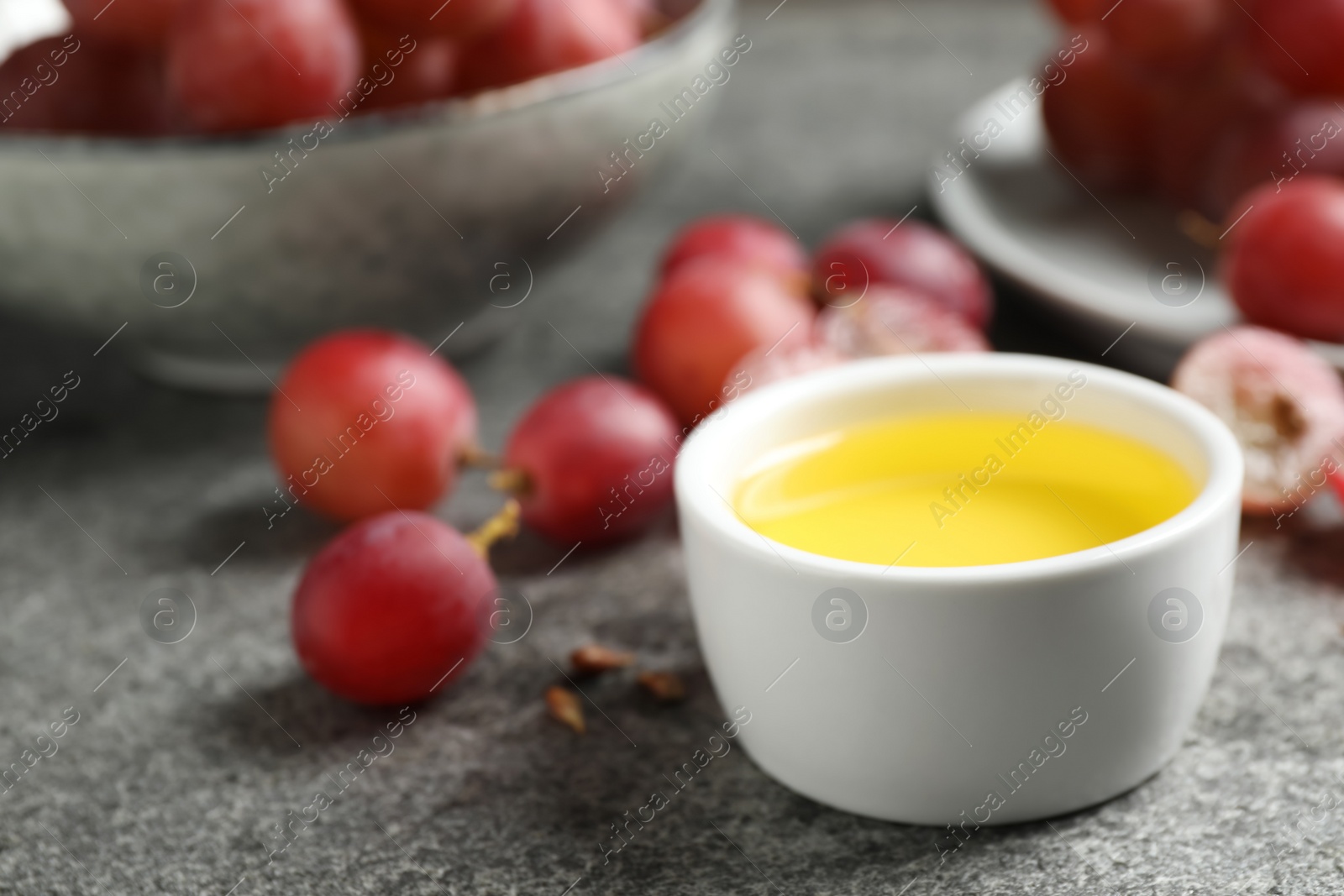 Photo of Bowl of natural grape seed oil on grey table. Organic cosmetic