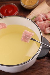 Photo of Fondue pot, fork, pieces of raw meat and sauces on wooden table, closeup