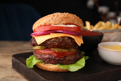 Photo of Tasty cheeseburger with patties, tomato and sauce on wooden table, closeup