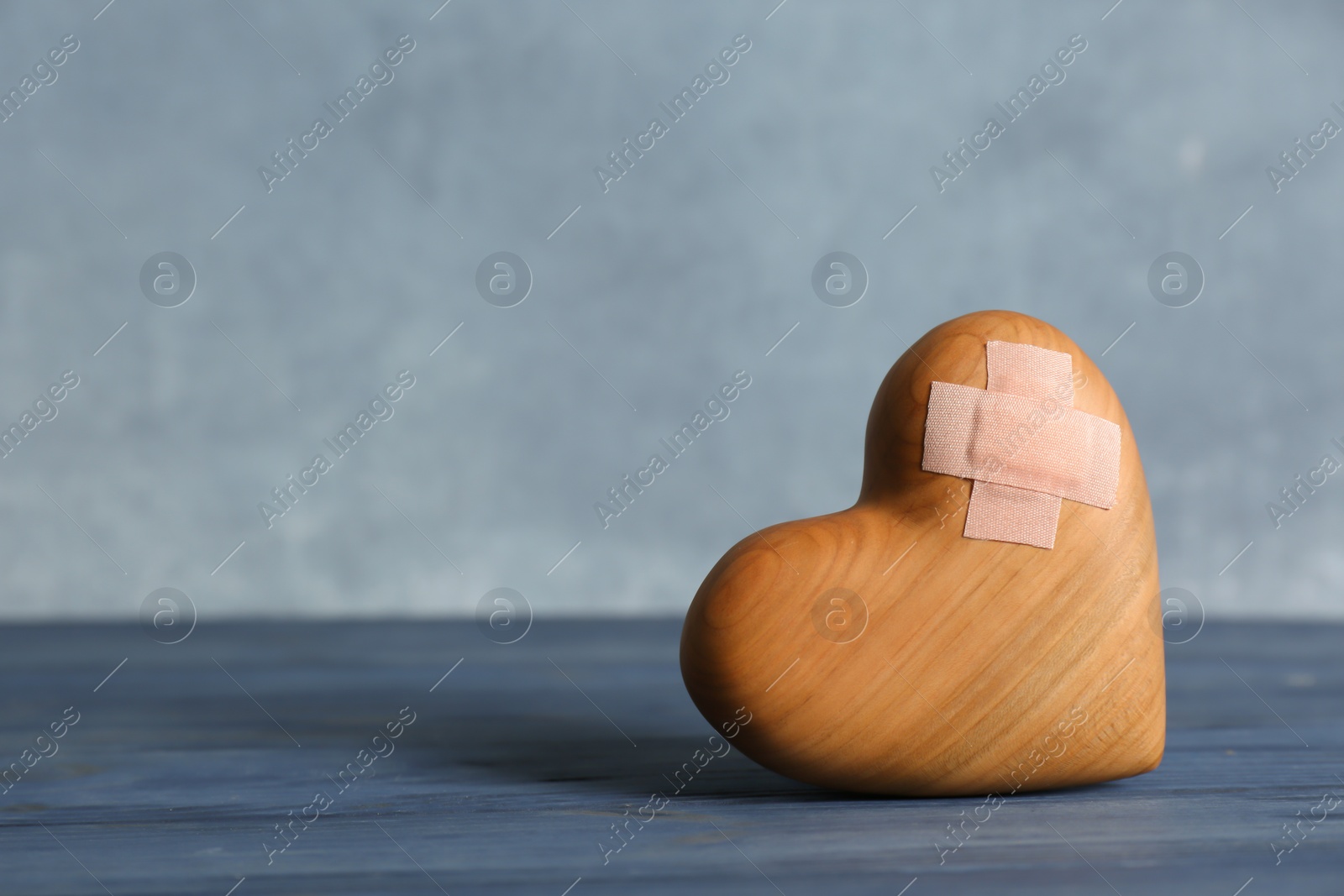 Photo of Wooden heart with adhesive plasters on table. Space for text