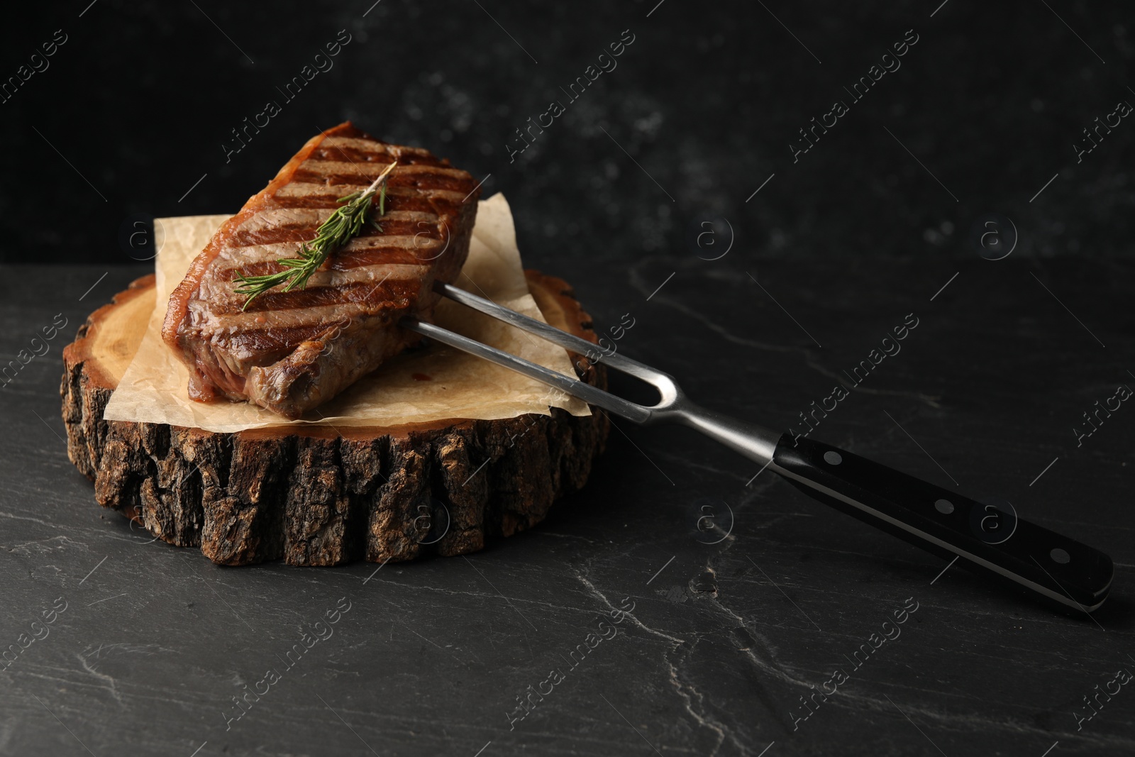 Photo of Delicious grilled beef steak served with rosemary on dark gray table