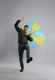 Photo of Emotional man with umbrella caught in gust of wind on grey background