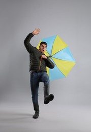 Emotional man with umbrella caught in gust of wind on grey background