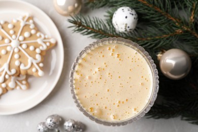 Photo of Glass of delicious eggnog, cookies and decorated fir branch on light table, flat lay