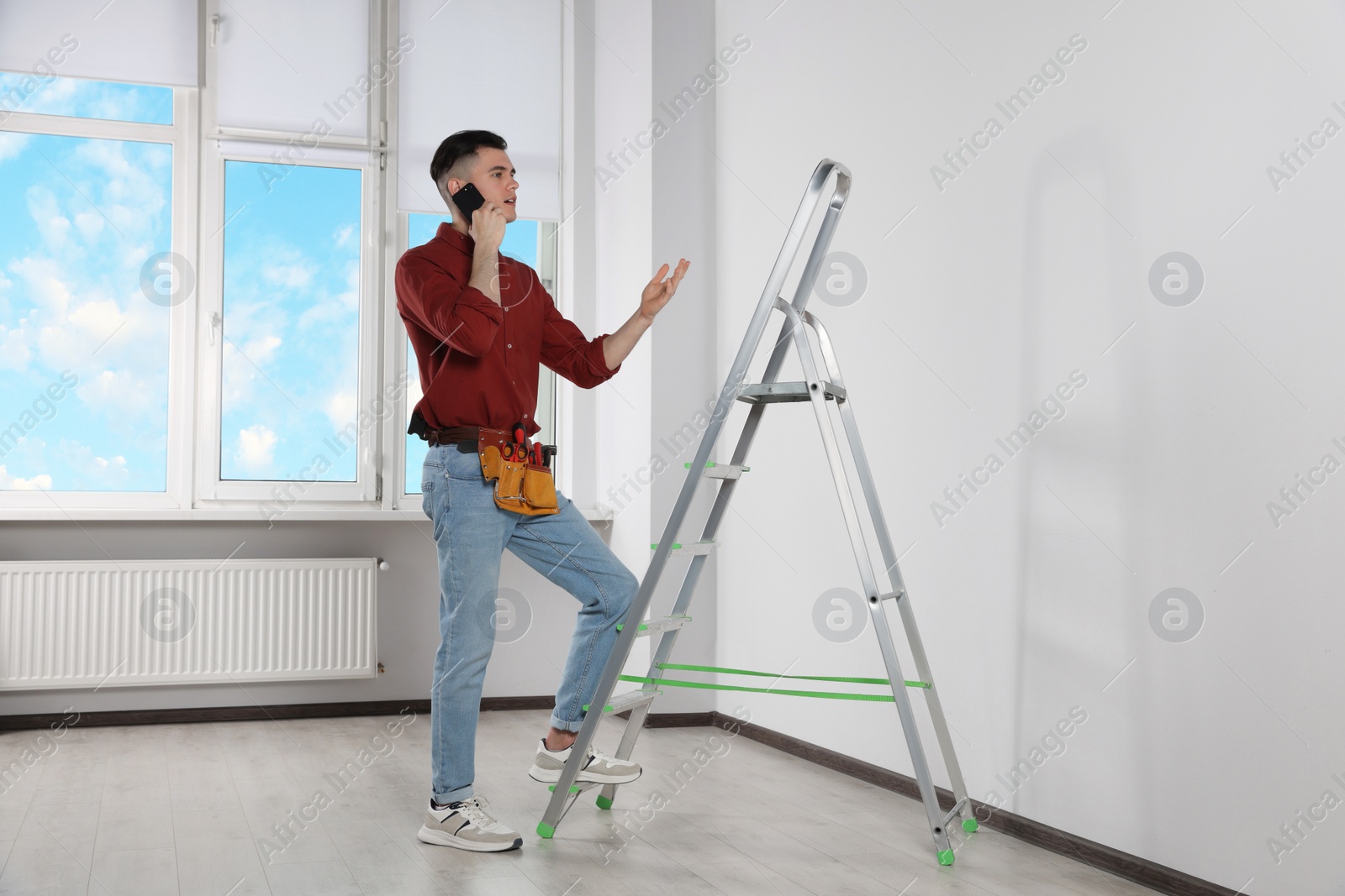 Photo of Handyman talking on phone while climbing up stepladder in room