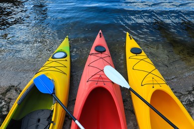 Photo of Modern kayaks with paddles on beach near river, above view. Summer camp activity