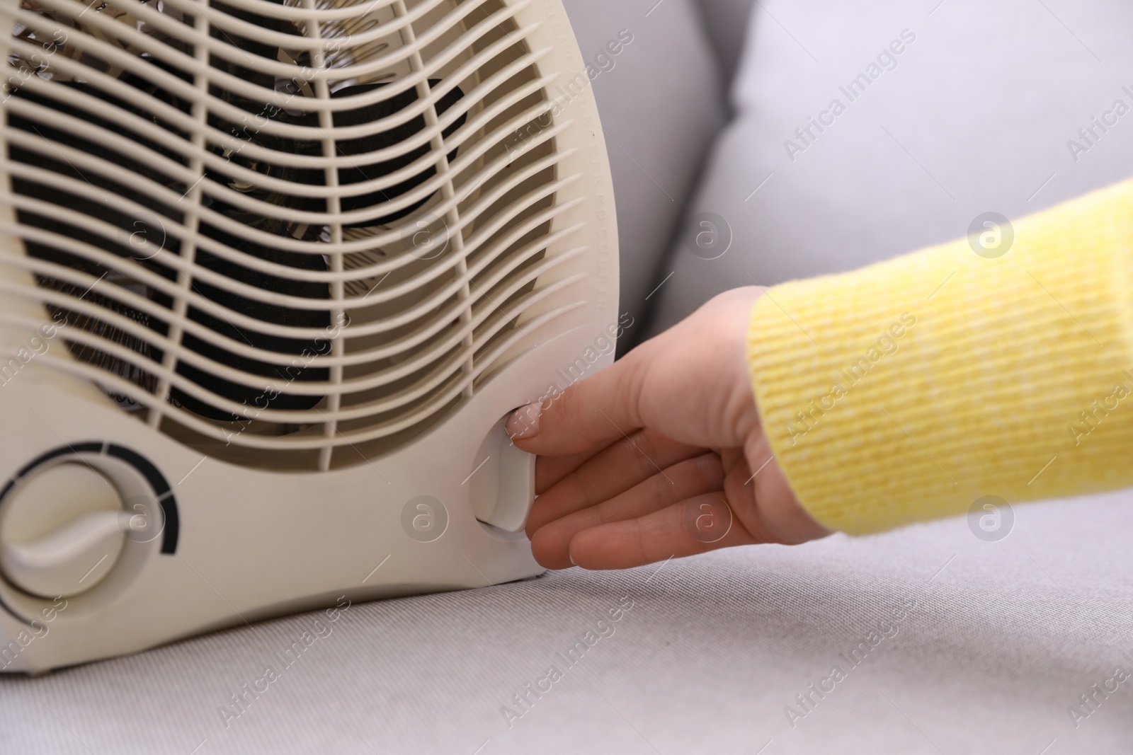 Photo of Woman turning on fan heater indoors, closeup