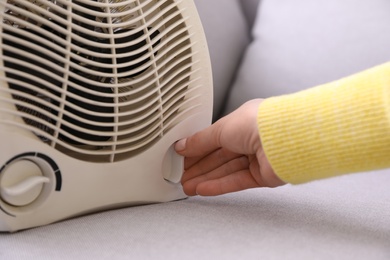 Photo of Woman turning on fan heater indoors, closeup
