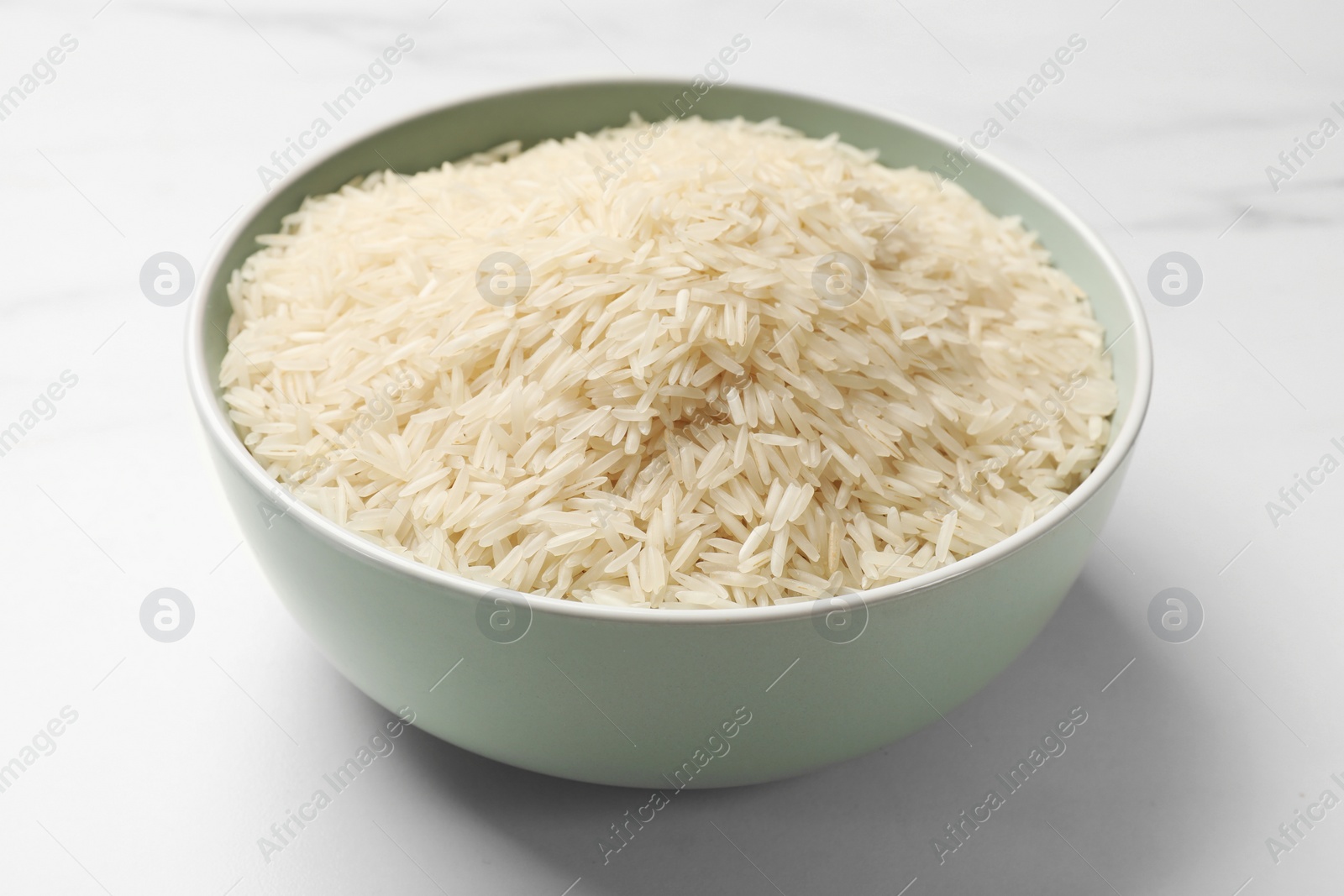 Photo of Raw basmati rice in bowl on white marble table