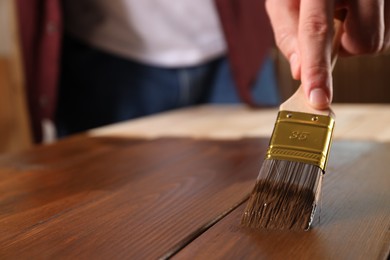 Man with brush applying wood stain onto wooden surface, closeup