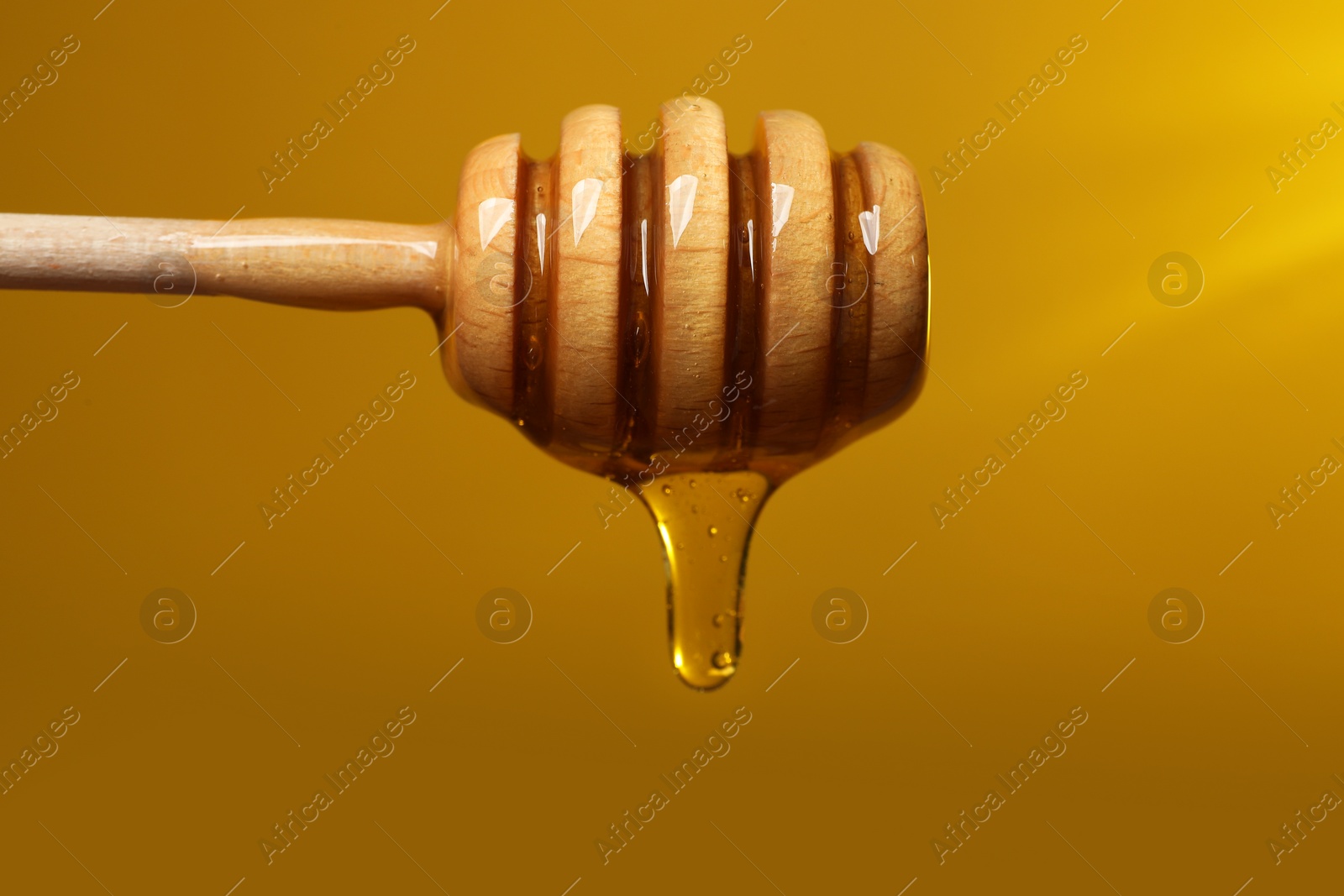 Photo of Pouring honey from dipper against golden background, closeup