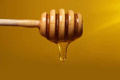 Photo of Pouring honey from dipper against golden background, closeup
