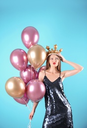 Young woman with crown and air balloons on color background