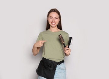 Portrait of happy hairdresser with brushes on light background