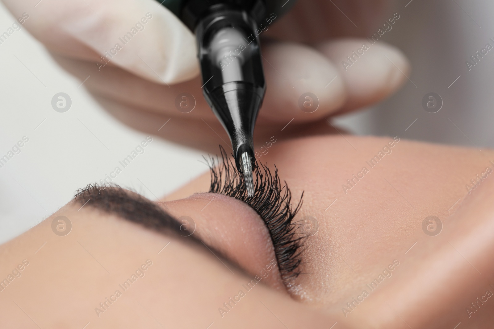 Photo of Young woman undergoing procedure of permanent eye makeup, closeup