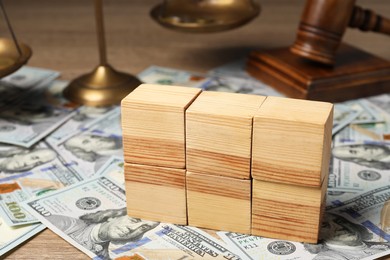 Photo of Tax law. Blank wooden cubes, dollar banknotes, gavel and scales on table, closeup