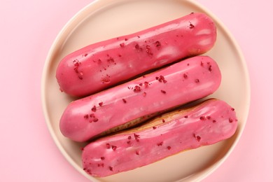 Delicious eclairs covered with glaze on pink background, top view